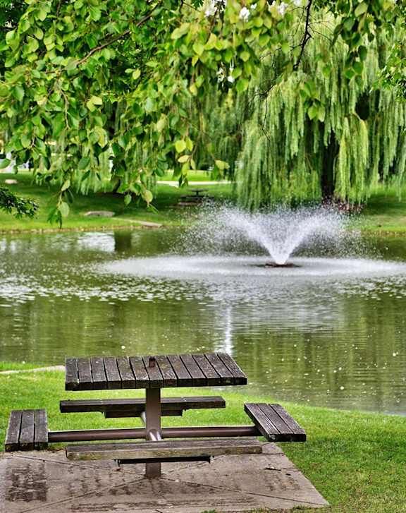 A picnic table is in front of a pond with a fountain.