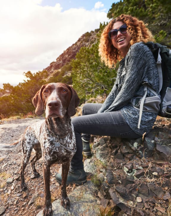 a woman and her dog sitting on a rock in the mountains