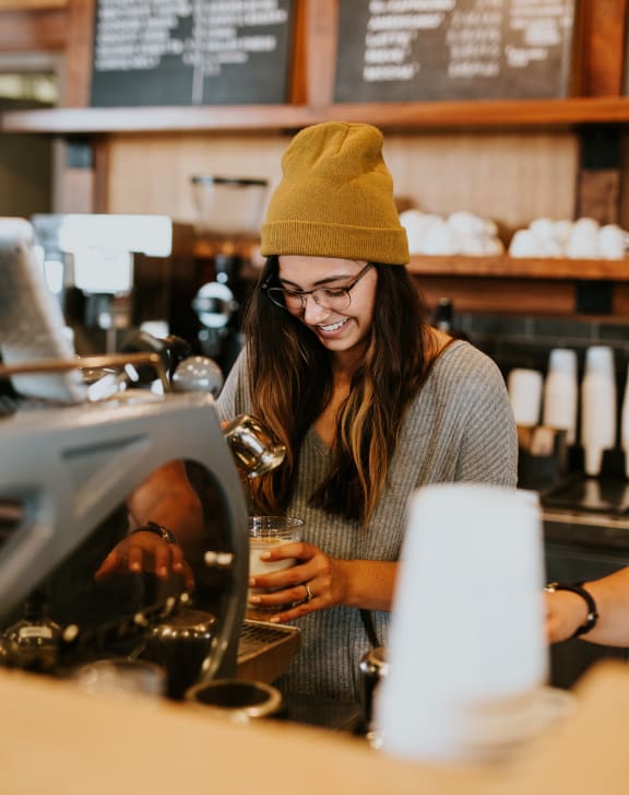 a woman in a beanie pouring a drink at a coffee shop