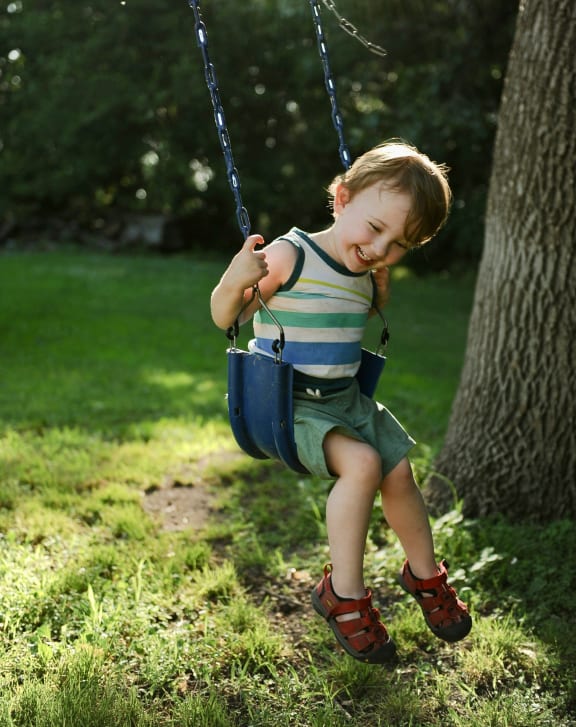 a little boy sitting on a swing in a park