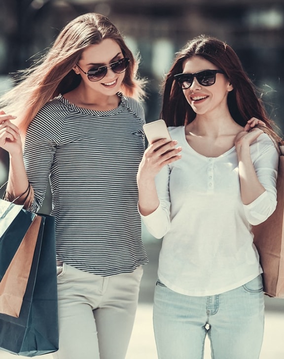 two women walking down the street with shopping bags and a cell phone at The Junction at Rogers, Rogers, 72756