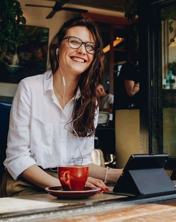 A woman in a white shirt is sitting at a table with a red cup and a black tablet.