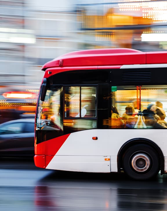 A red and white bus is in motion on a wet street.