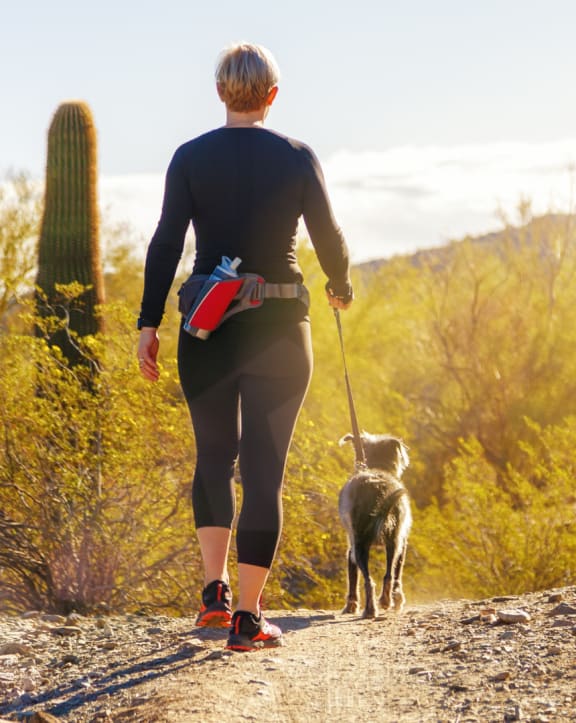 a woman walking her dog on a trail in the desert
