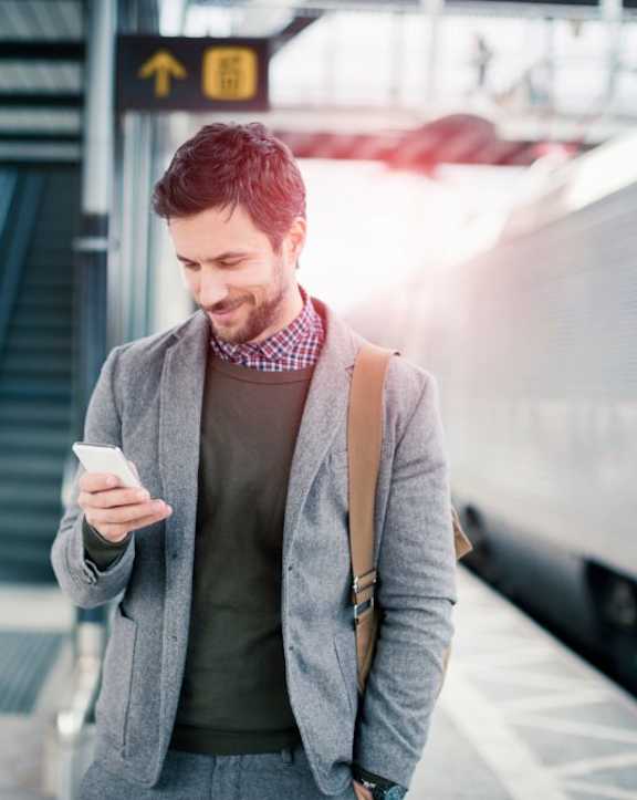 A man is standing on a train platform looking at his phone.