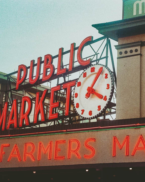 a large clock on the top of a farmers market sign