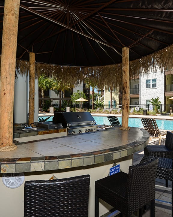 a bar with a grill next to a swimming pool with a building in the background at Cabana Club Apartments in Jacksonville, Florida 32256