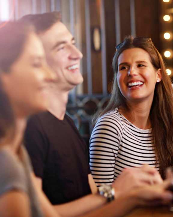 Four people are sitting at a bar, smiling and enjoying drinks.