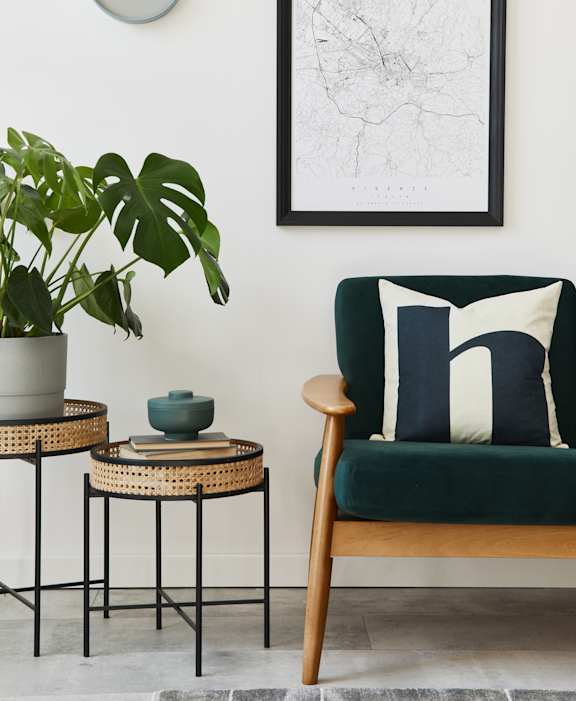 A living room with a green chair, a potted plant, and a framed map on the wall.