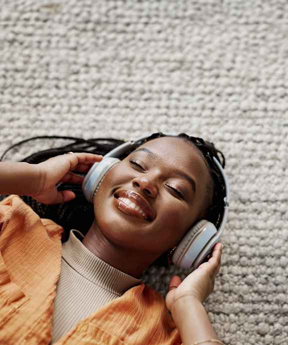 A person wearing headphones and an orange top is lying down on a textured surface.