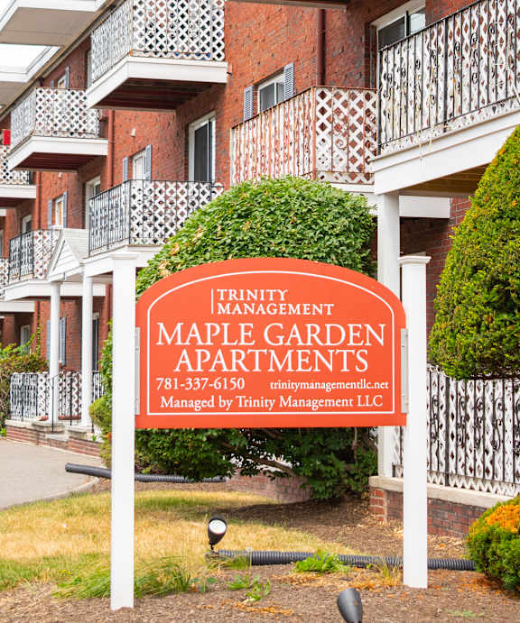 A red brick apartment building with a sign that says Maple Garden Apartments.