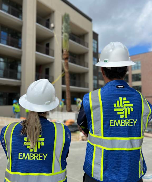 Two construction workers wearing safety vests with the name "Embrey" on them.