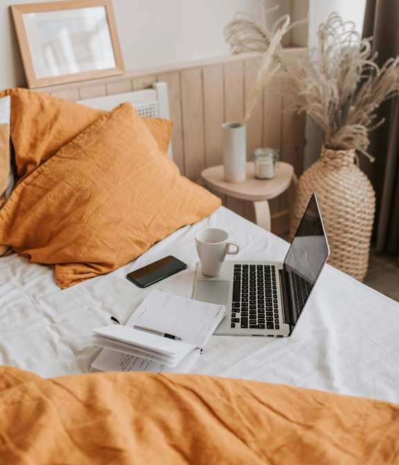 A bed with a laptop, a cup, and some papers on it.