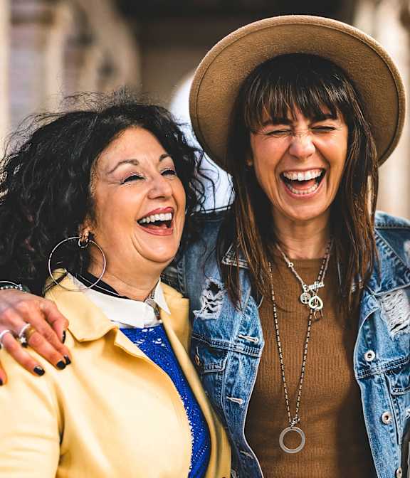 Two women laughing together with one wearing a hat.
