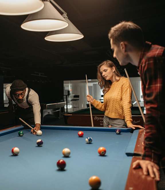 Three people playing pool in a dark room.