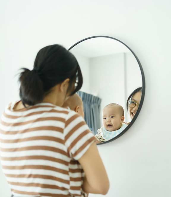 A woman in a striped shirt is looking at her reflection in a round mirror. at Townhomes at Preserve, Rogers, Minnesota