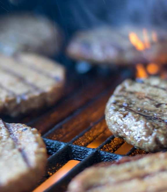 A close up of four hamburgers cooking on a grill.