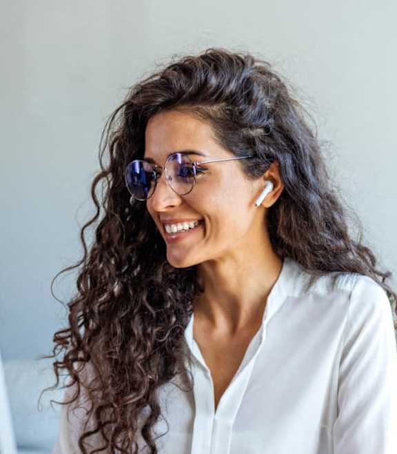 A woman with curly hair is wearing sunglasses and a white shirt while using a computer.