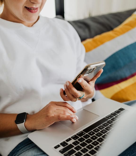 a woman sitting on a couch using her laptop computer and cell phone