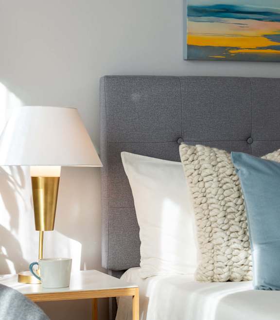 A bed with a grey headboard and white pillows with blue and white stripes