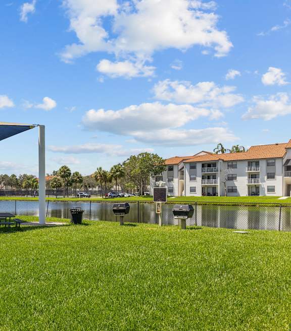 A blue and white shade structure sits in a grassy field next to a body of water.