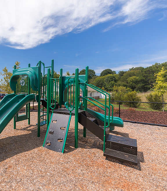 A green playground slide in the middle of a playground.