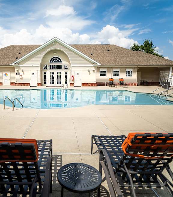 A pool with a building behind it and chairs in front.