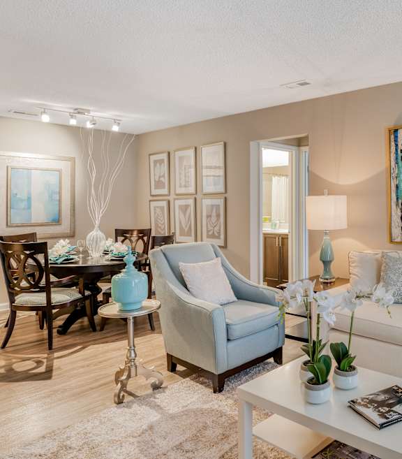 A living room with a white couch, a coffee table, a dining table, and a painting on the wall.