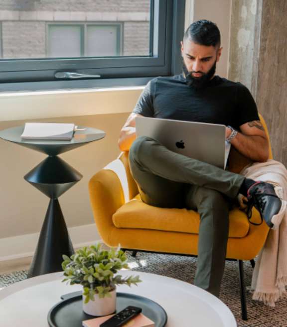 A Man sitting on yellow chair and working on laptop at Coda on Half Apartments, District of Columbia, 20003