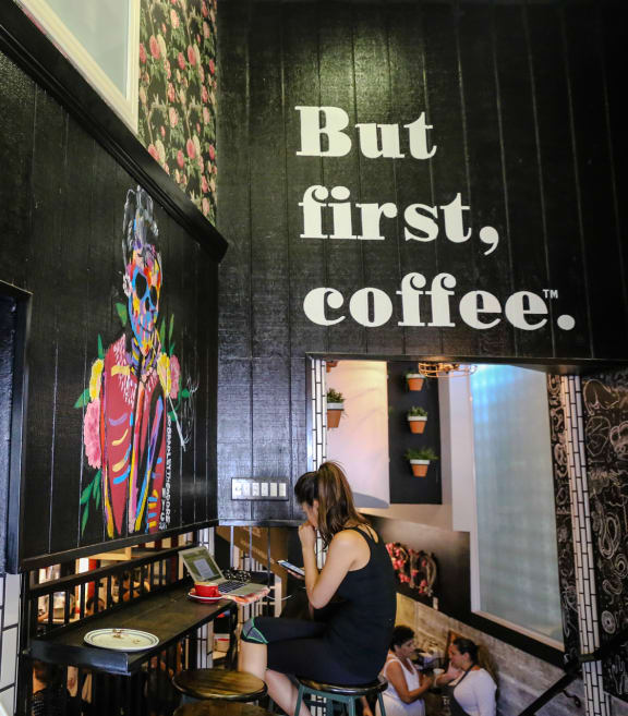 a woman sitting at a bar in a coffee shop with a sign on the wall