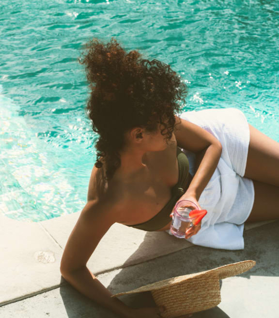 a woman sitting by a pool drinking a cocktail
