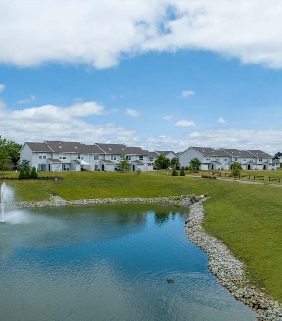 A fountain in the middle of a pond in front of a row of houses.