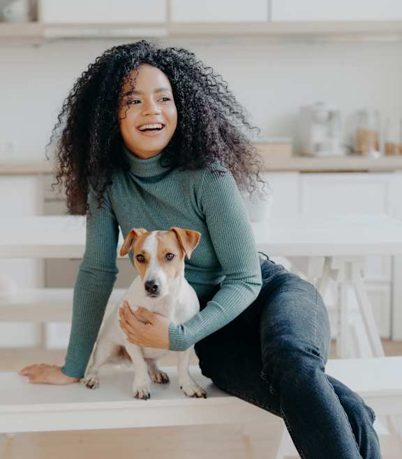A woman with curly hair is sitting on a white table with a small dog in her lap. at The Cunningham Apartments, Iowa