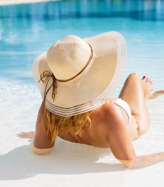 a woman laying in the water at the beach wearing a hat