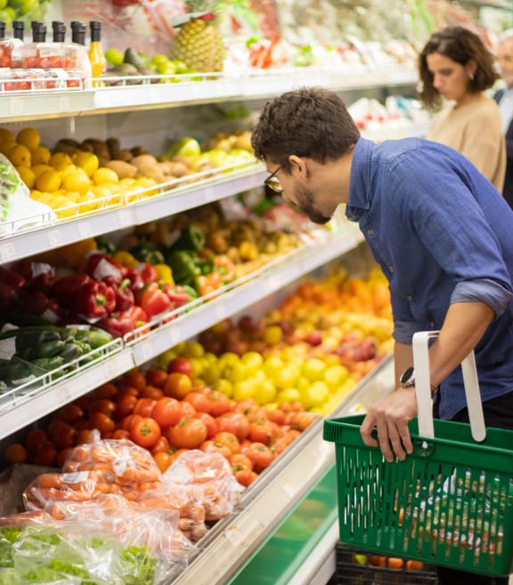a man carrying a green shopping basket in a grocery store