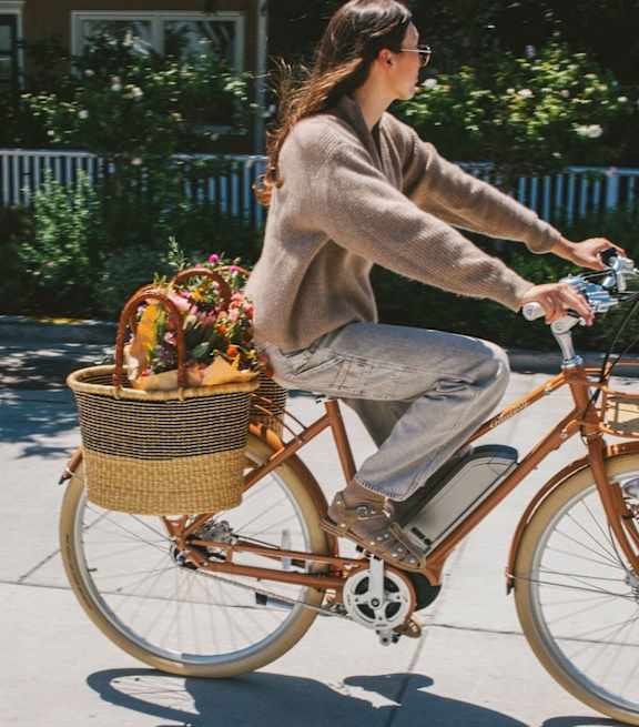 A woman riding a bike with a basket full of flowers.