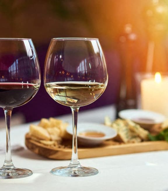 two glasses of red and white wine sitting on a table with a tray of food  at The Meadows, Georgia, 31302