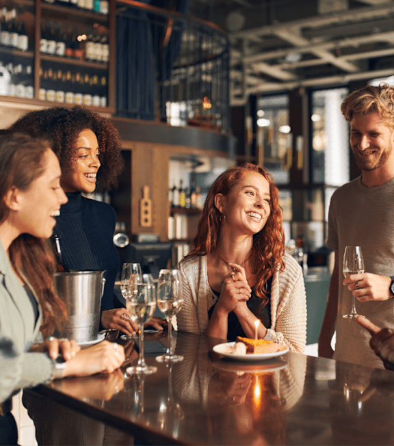 A group of people are gathered around a bar counter, enjoying drinks and conversation.