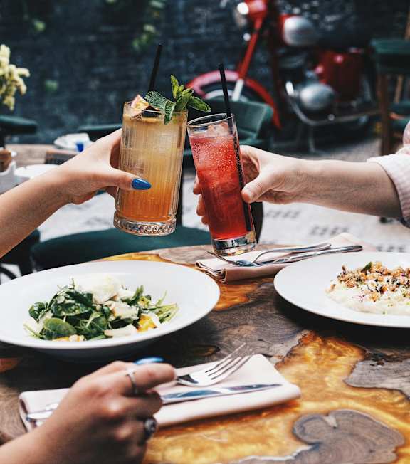 Two people toasting with drinks at a table with food at Pines at Lawrenceville Apartments in Decatur, GA, 30033