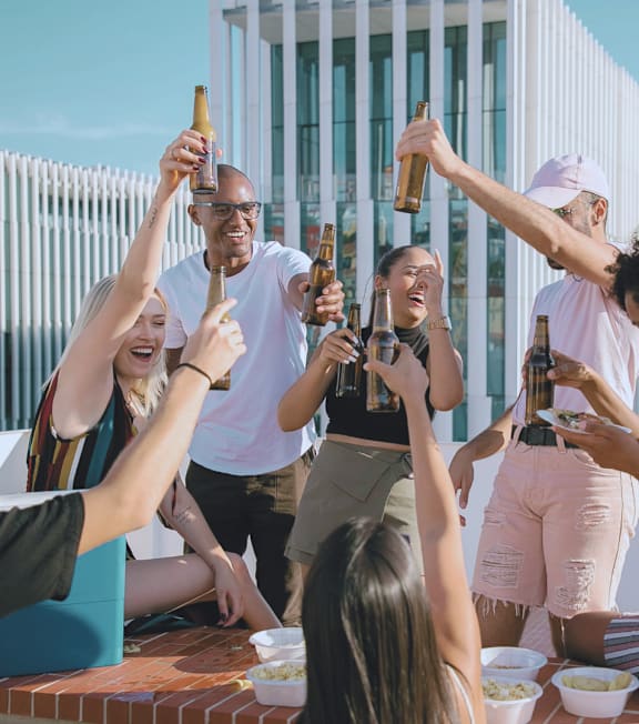 A group of people are toasting with beer bottles on a rooftop.