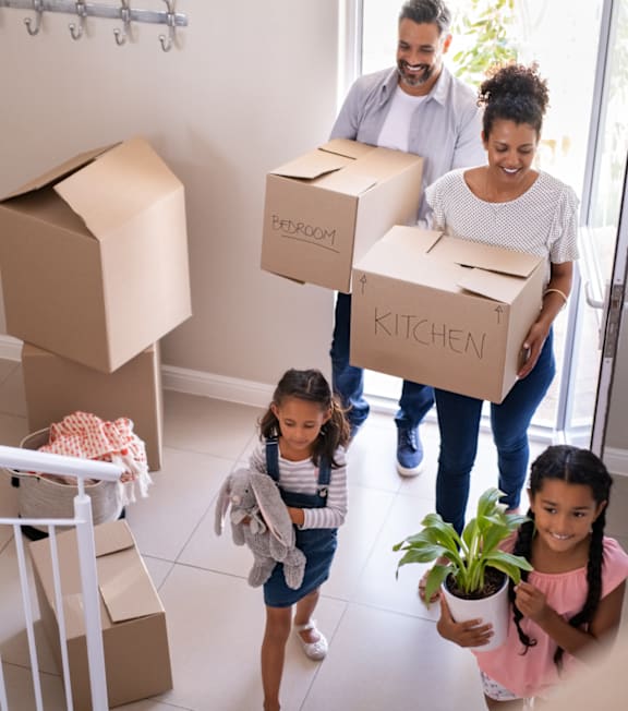 A family moving into a new home, carrying boxes labeled "kitchen" and "bedroom".