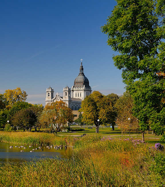 A beautiful landscape with a lake, trees, and a large building in the background.