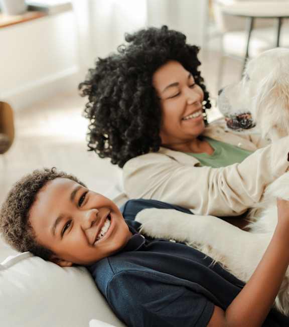 A woman and two children are cuddling a white dog on a couch.
