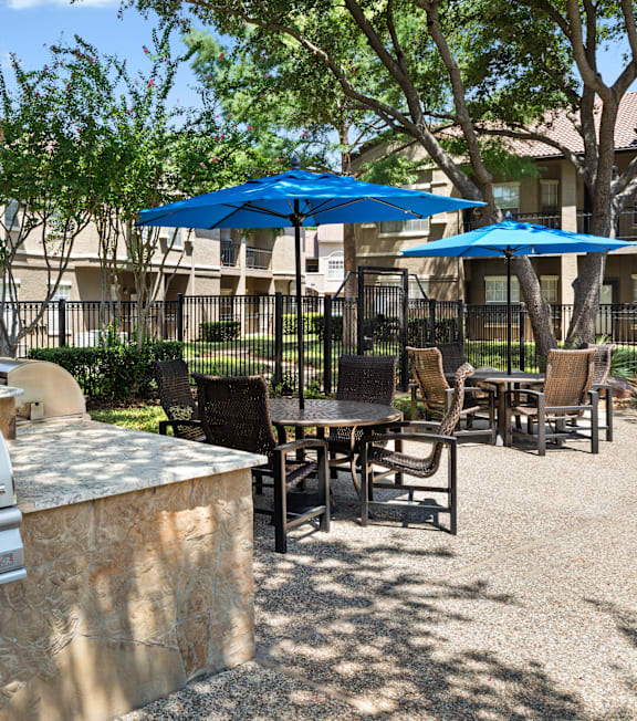 A BBQ grill is in the middle of a patio with chairs and umbrellas.