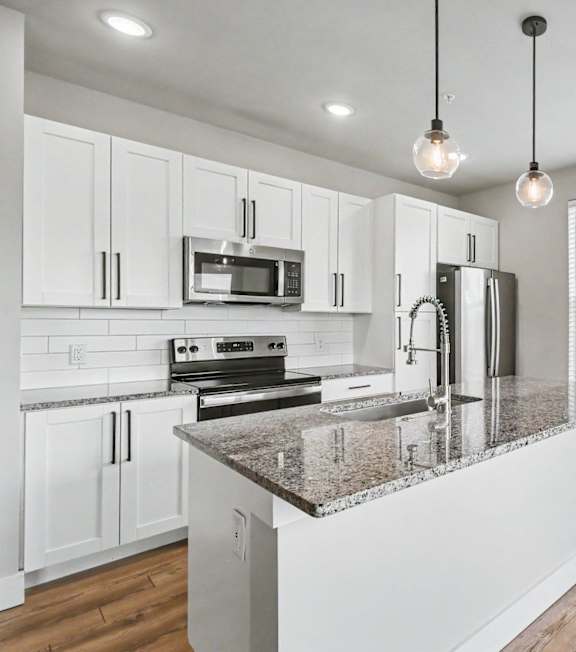 A modern kitchen with a granite countertop and stainless steel appliances at The Oliver Apartments, Olivette, MO, 63132