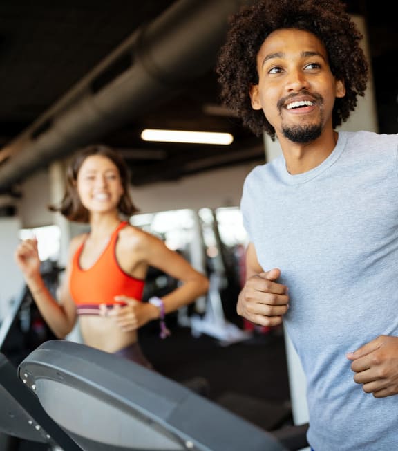 a man running on a treadmill at a gym with a woman in the background at Studebaker Lofts, South Bend, IN, 46601