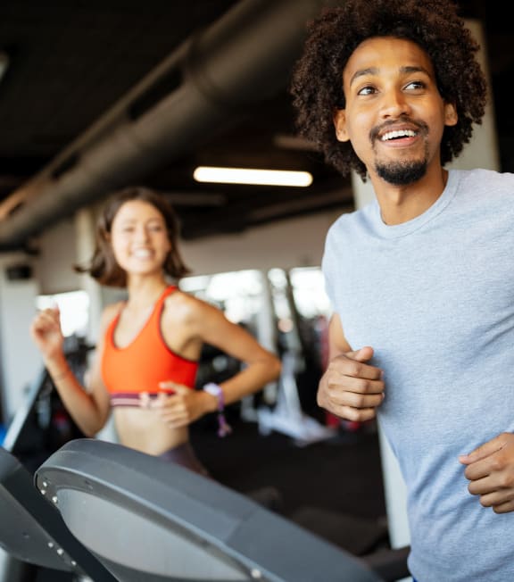 a man running on a treadmill at a gym with a woman in the background at The Rail, St. Louis, MO