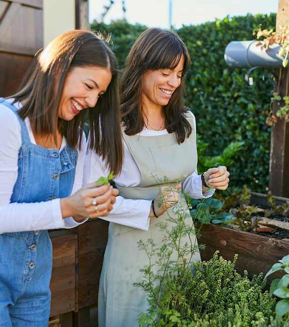 Two women are standing in a garden, one is wearing a denim jumpsuit and the other is wearing a white dress at Fernlow Apartments, Houghton Regis