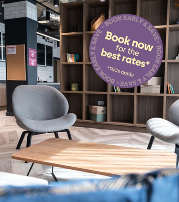 A room with a grey chair, a wooden table, and a bookshelf with a heart-shaped sticker on it.