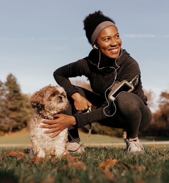a woman kneels down to pet her dog while listening to music on her headphones